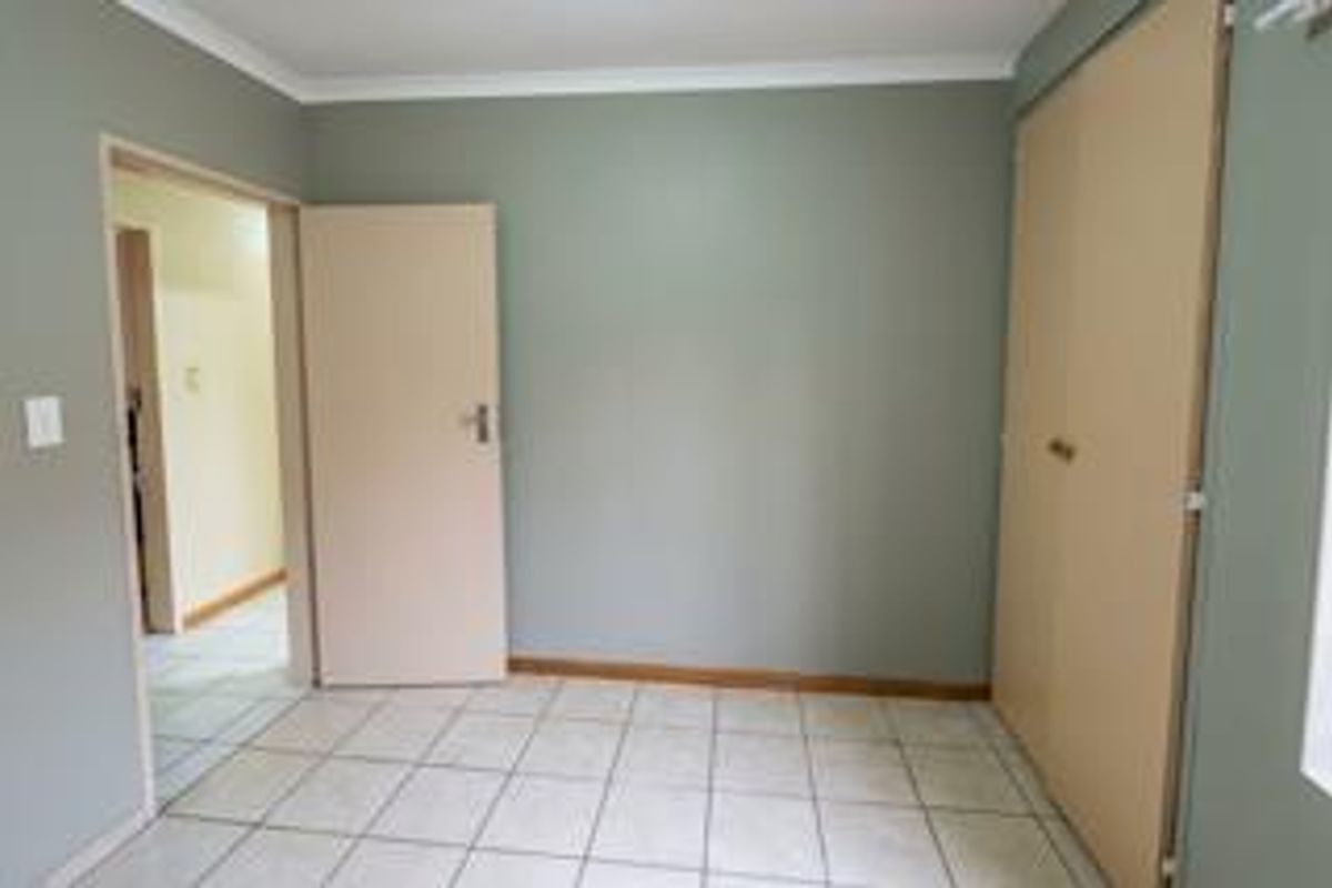 A clean, empty bedroom featuring neutral wall tones, tiled flooring, and built-in storage cupboards.
