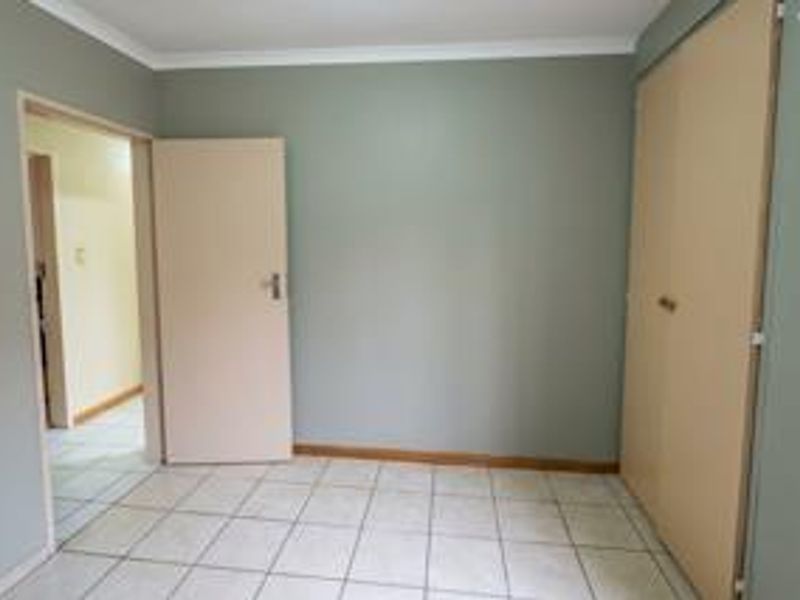 A clean, empty bedroom featuring neutral wall tones, tiled flooring, and built-in storage cupboards.