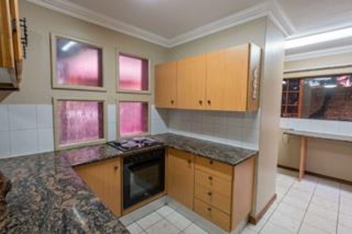 A functional kitchen featuring built-in wooden cabinetry, granite countertops, a built-in oven and hob, and tiled flooring with a neutral backsplash.