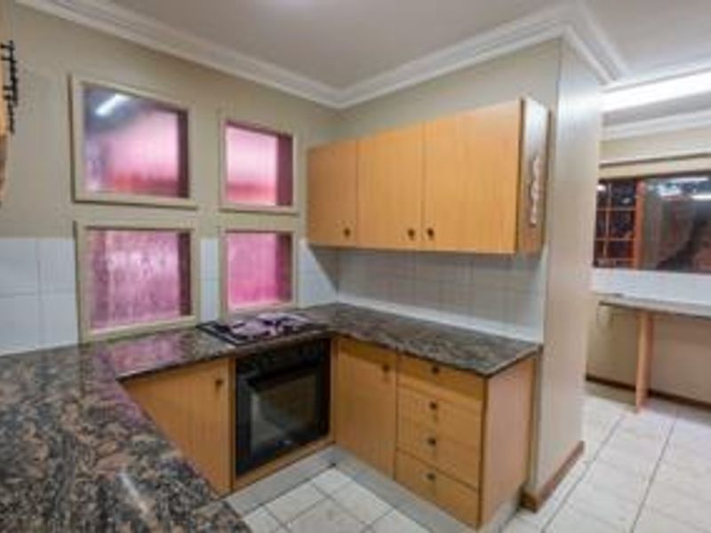 A functional kitchen featuring built-in wooden cabinetry, granite countertops, a built-in oven and hob, and tiled flooring with a neutral backsplash.