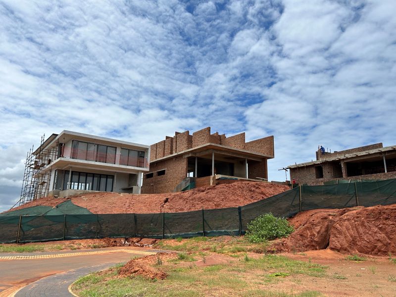 A multi-level townhouse development currently under construction, featuring exposed brickwork, concrete balconies, and large glass sliding doors in a developing estate.