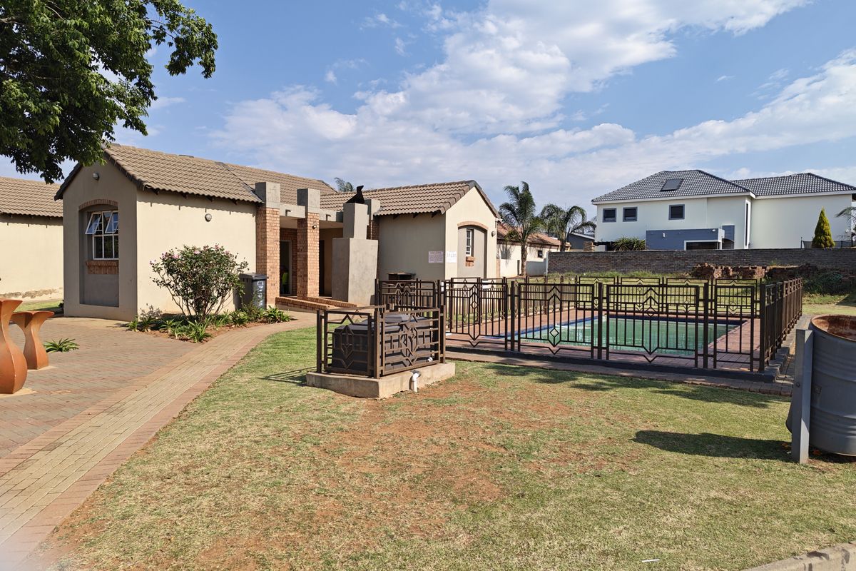 Rear exterior view featuring a swimming pool with metal safety fencing, paved walkways, and a built-in braai area set within a landscaped garden.
