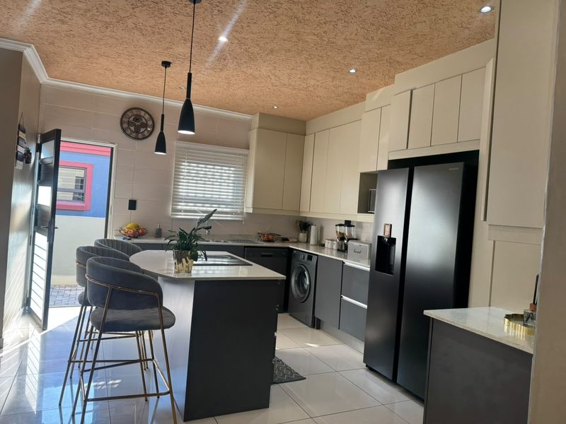 Modern kitchen featuring sleek cabinetry, stone countertops, a central island with breakfast bar seating, and integrated appliances, finished with contemporary lighting and tiled floors.