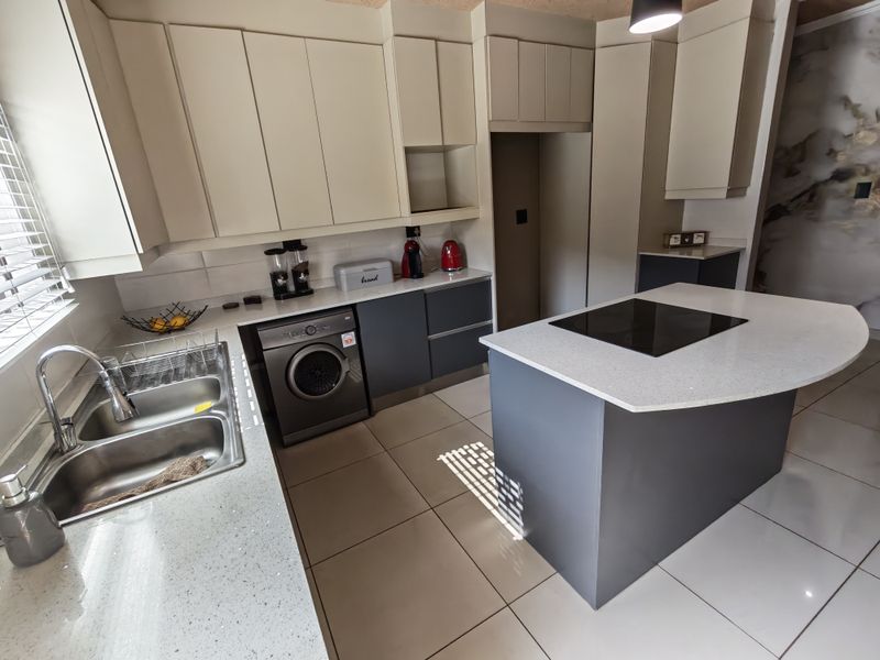 Modern kitchen featuring two-tone cabinetry, stone countertops, a central island with an integrated induction hob, and tiled flooring.