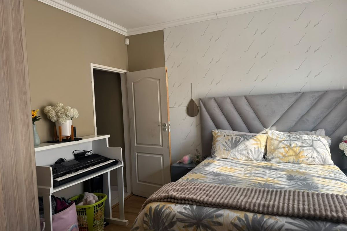 A bedroom featuring laminate flooring, recessed downlights, and decorative coving, with a feature wall behind the bed area.