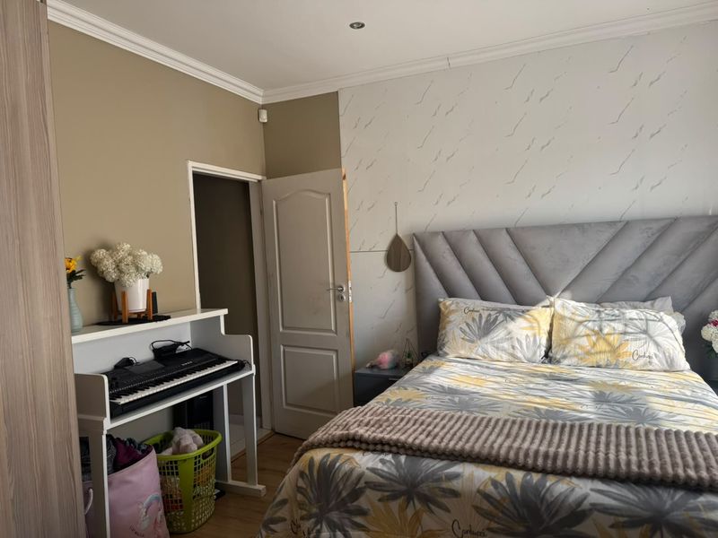 A bedroom featuring laminate flooring, recessed downlights, and decorative coving, with a feature wall behind the bed area.