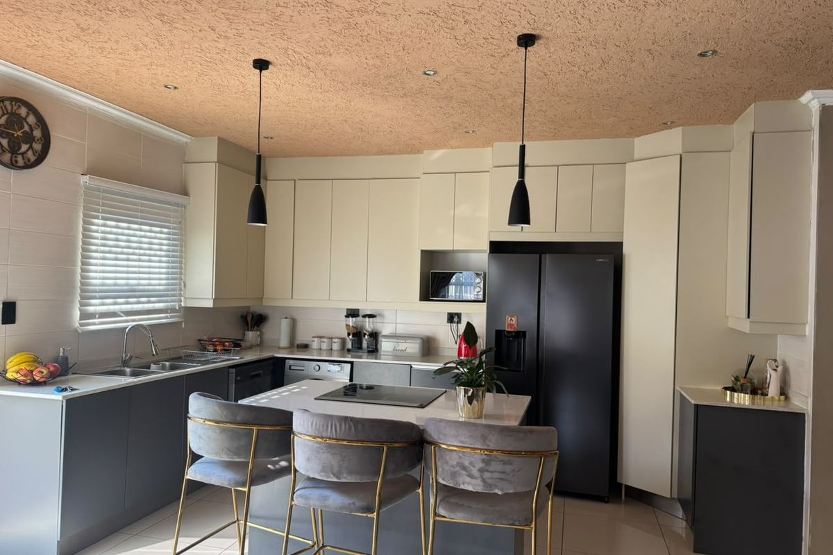 Modern kitchen featuring two-tone cabinetry, a central island with integrated hob, stone countertops, and contemporary pendant lighting.