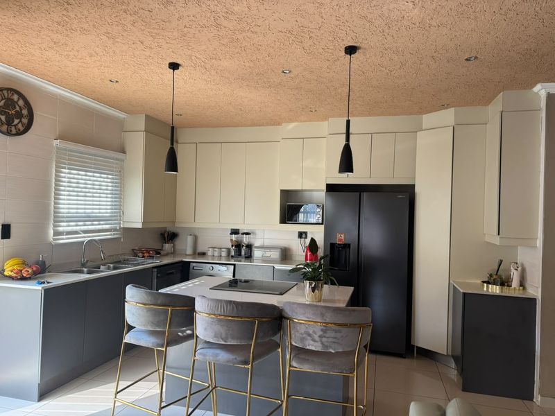 Modern kitchen featuring two-tone cabinetry, a central island with integrated hob, stone countertops, and contemporary pendant lighting.