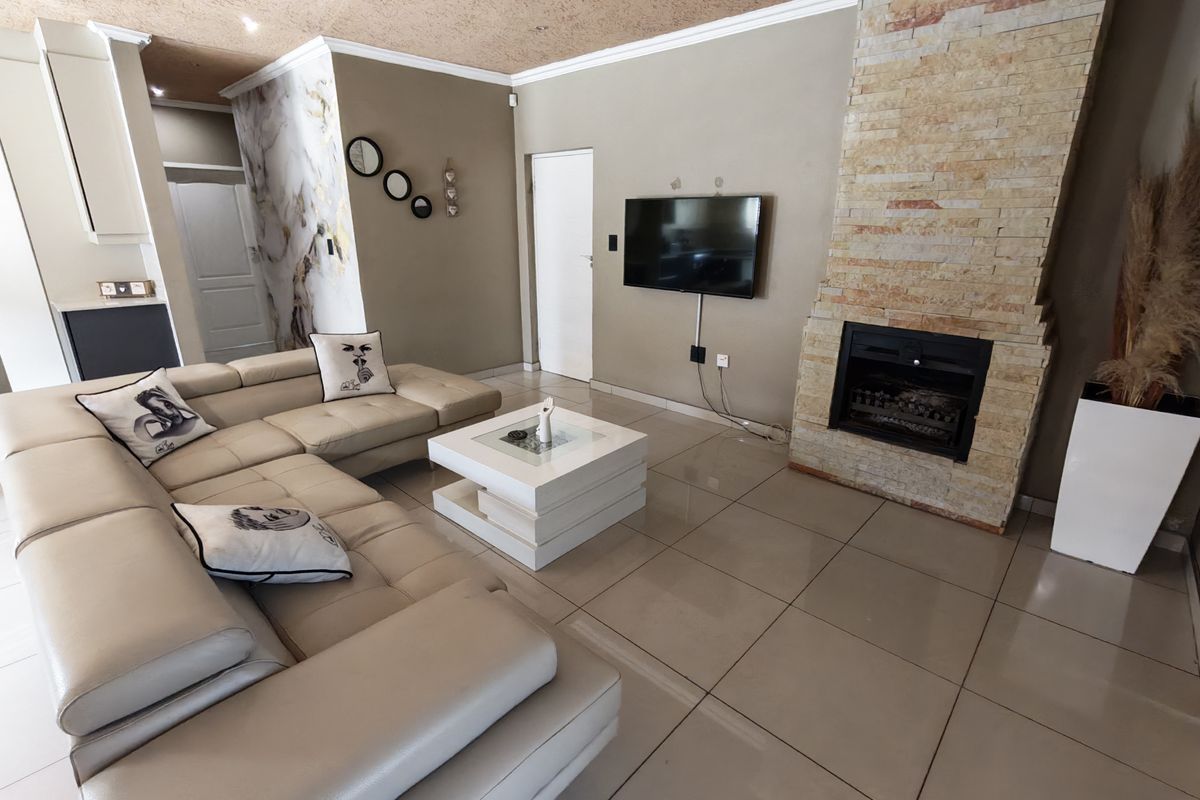 Spacious living room featuring a prominent stone-clad fireplace, large format floor tiles, and recessed ceiling lighting, creating a comfortable and modern atmosphere.