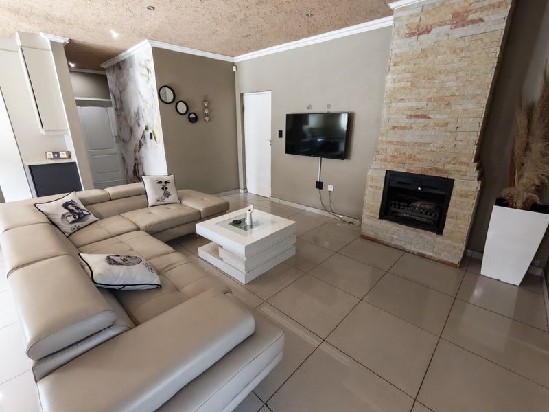 Spacious living room featuring a prominent stone-clad fireplace, large format floor tiles, and recessed ceiling lighting, creating a comfortable and modern atmosphere.