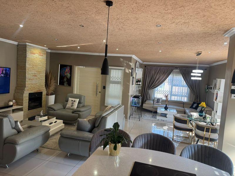 Spacious open-plan living and dining area featuring a stone-clad fireplace, modern tiled flooring, and recessed lighting throughout the main living space.
