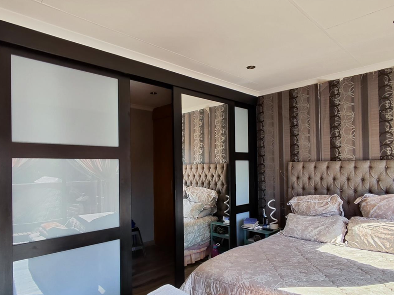 A well-maintained bedroom featuring a large built-in sliding door wardrobe with a combination of frosted glass and mirrored panels, complemented by recessed ceiling lighting.