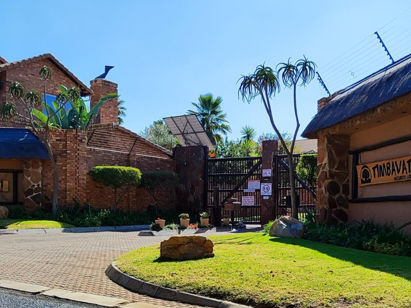 Front entrance view of Timbavati Security Lodge featuring a brick facade, thatched roof elements, secure gated access, and well-maintained landscaped gardens.