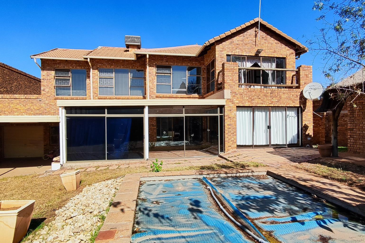 Rear view of a double-story face brick house featuring a swimming pool, covered patio, balcony, and integrated garage.