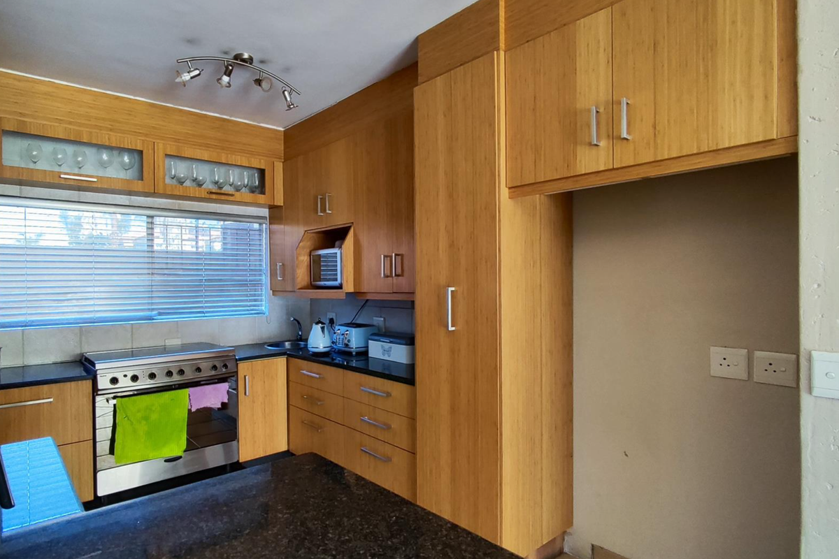 A functional kitchen featuring warm-toned wooden cabinetry, granite countertops, a built-in stove, and ample storage space with a dedicated refrigerator alcove.