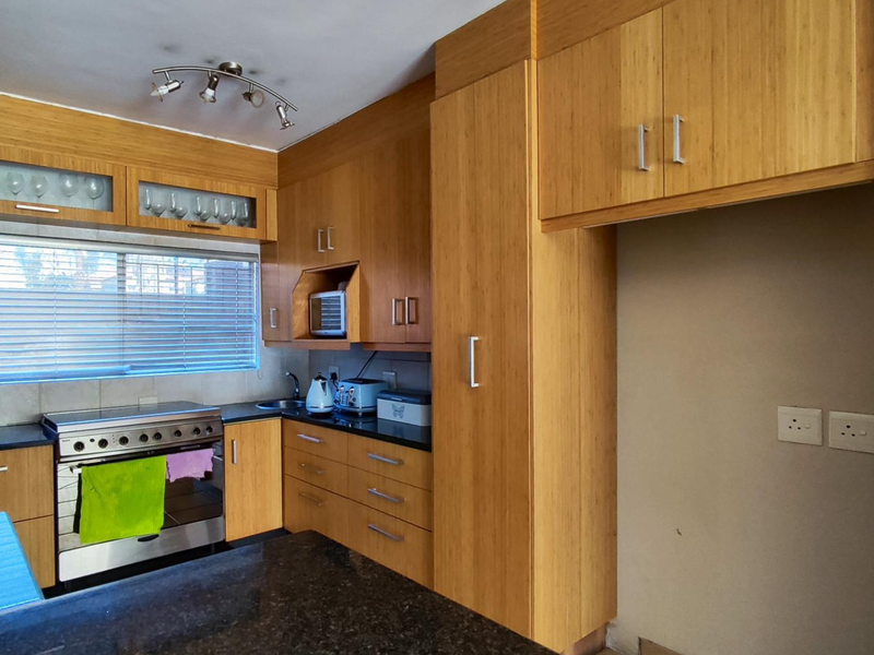 A functional kitchen featuring warm-toned wooden cabinetry, granite countertops, a built-in stove, and ample storage space with a dedicated refrigerator alcove.