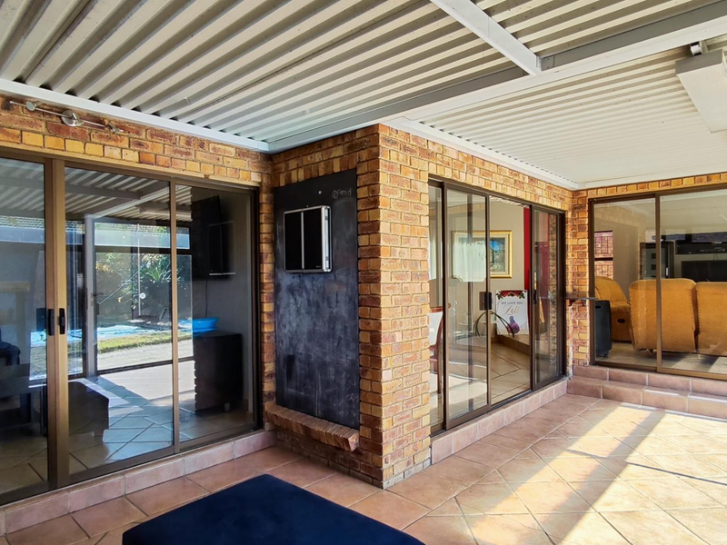 A spacious covered patio featuring durable tiled flooring, face brick walls, and multiple sliding glass doors providing seamless access to the interior living areas.