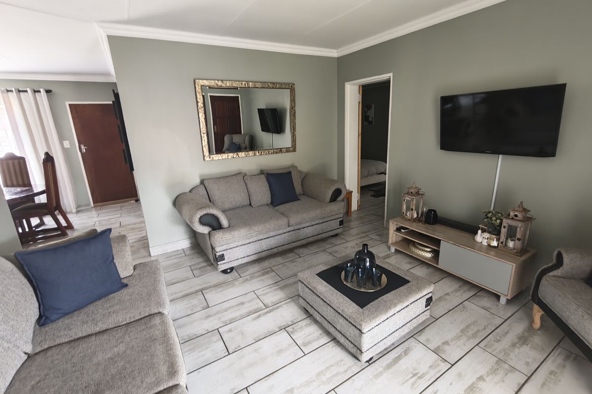 A well-maintained living room featuring light-toned tiled flooring, neutral wall paint, and classic ceiling cornicing, creating a comfortable and inviting atmosphere.