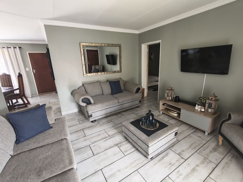 A well-maintained living room featuring light-toned tiled flooring, neutral wall paint, and classic ceiling cornicing, creating a comfortable and inviting atmosphere.