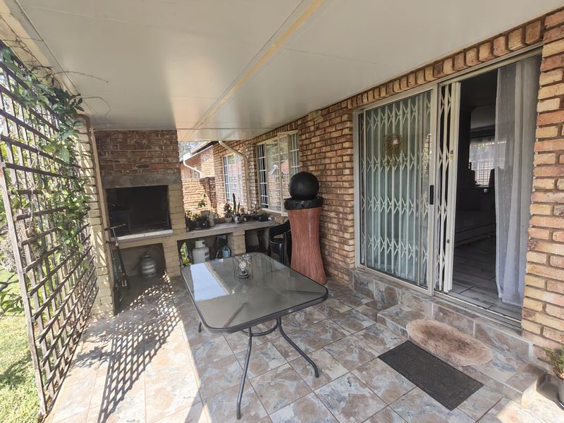 Covered patio area featuring a built-in brick braai, tiled flooring, and direct access to the interior through a sliding glass door with security gate.