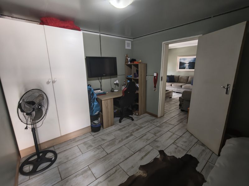 A bedroom featuring tiled flooring and a built-in wardrobe, with a doorway leading into an adjacent living area.