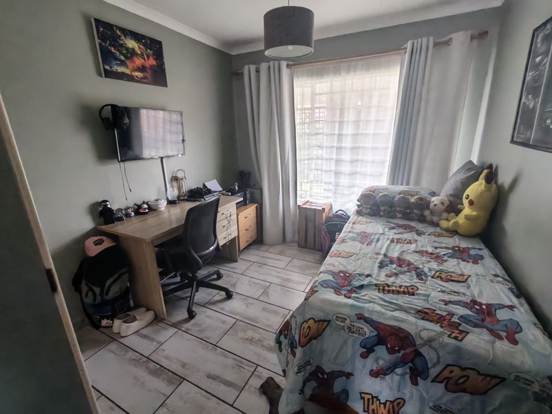 A functional bedroom featuring tiled flooring, a window with curtain treatments, and a central ceiling light fixture.