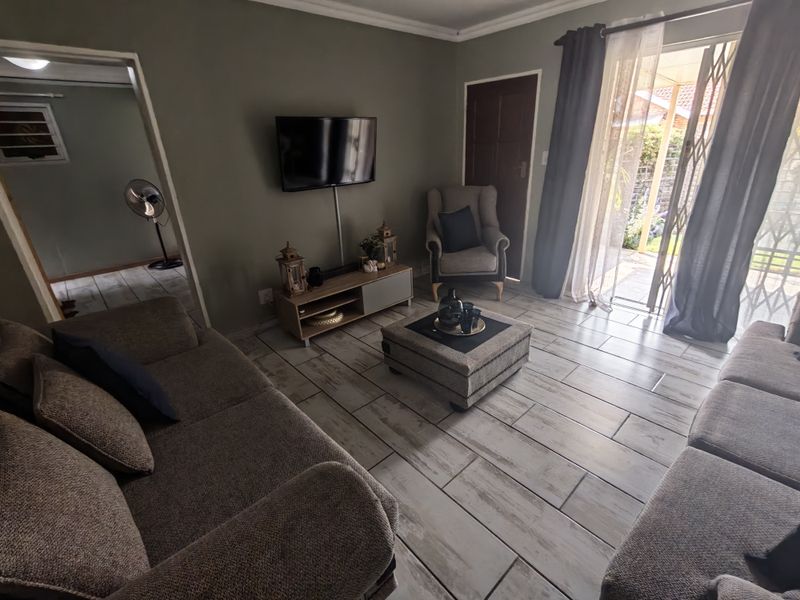 A comfortable living room featuring tiled flooring, coving, and a sliding glass door with a security gate providing access to the outdoor area.