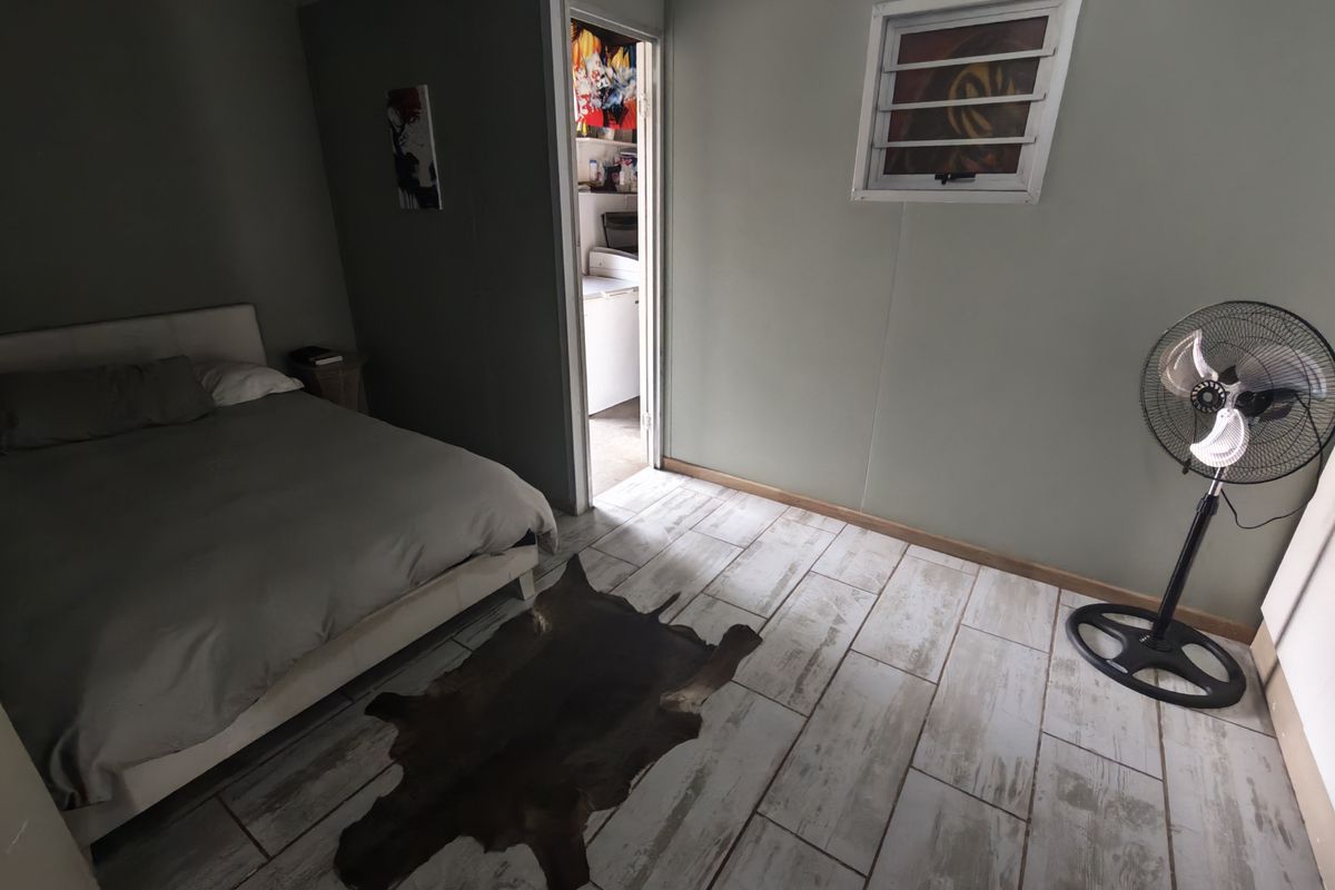 A bedroom featuring tiled flooring and a louver window, with an adjacent doorway leading to a secondary utility or kitchen area.