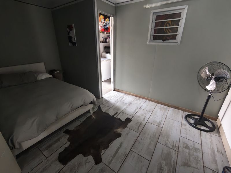 A bedroom featuring tiled flooring and a louver window, with an adjacent doorway leading to a secondary utility or kitchen area.