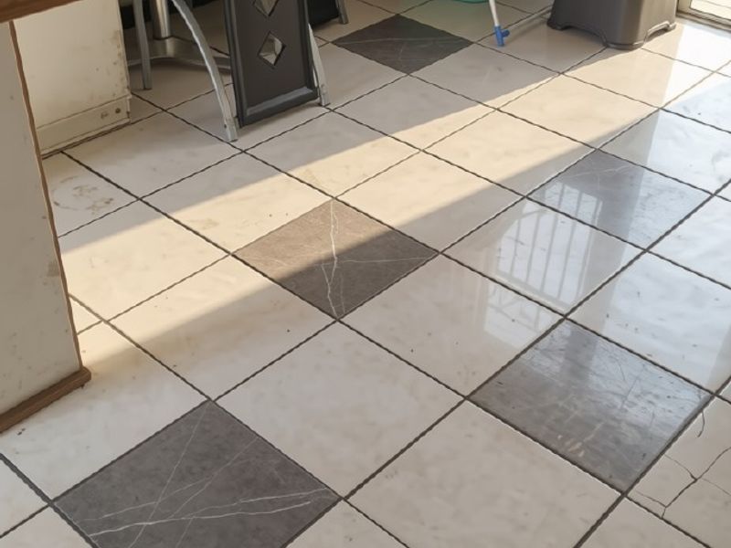 A kitchen area featuring a checkered tile floor with visible cracks and wear, leading to a sliding glass door.