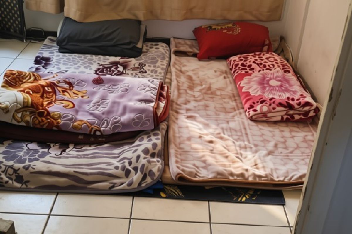 A small bedroom space featuring tiled flooring and a window, currently used as a sleeping area.