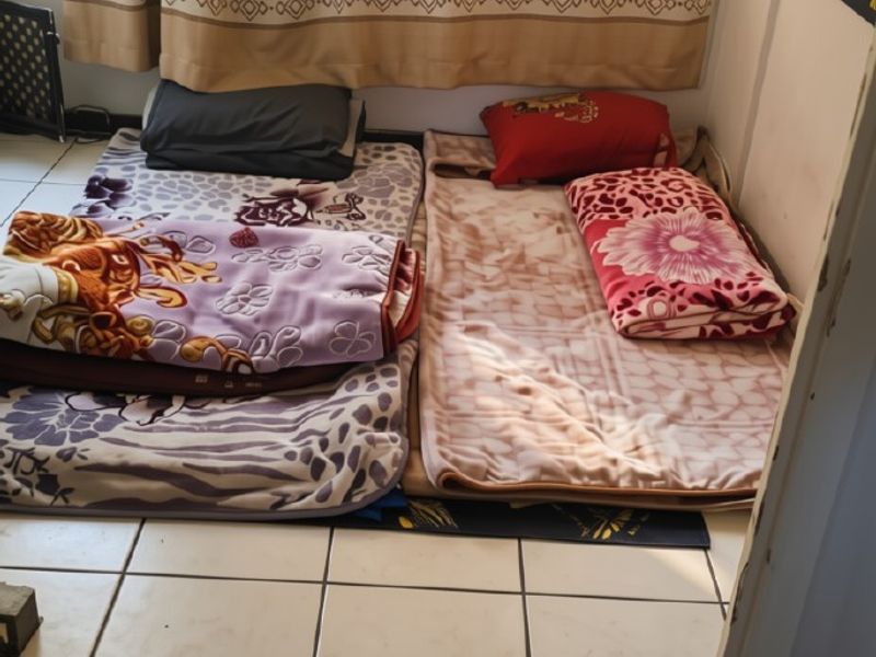 A small bedroom space featuring tiled flooring and a window, currently used as a sleeping area.