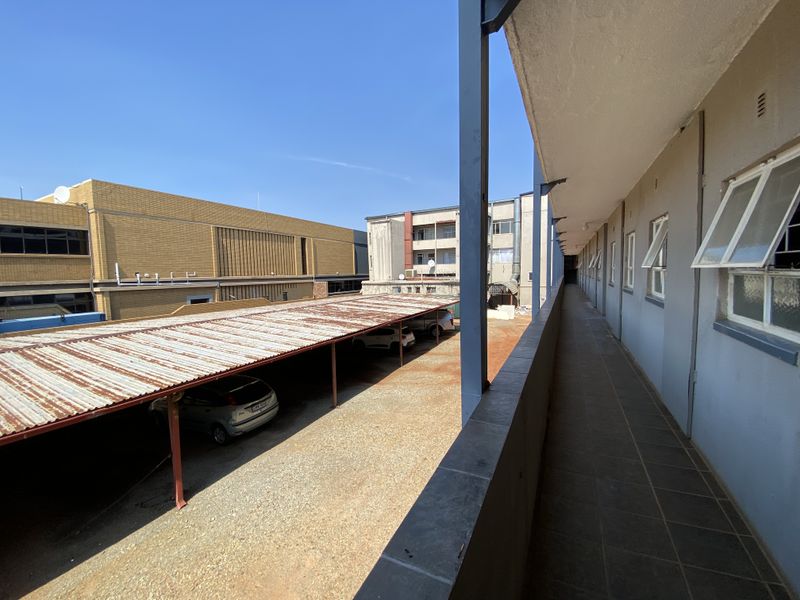 An elevated exterior walkway overlooking a parking area with a metal carport structure.