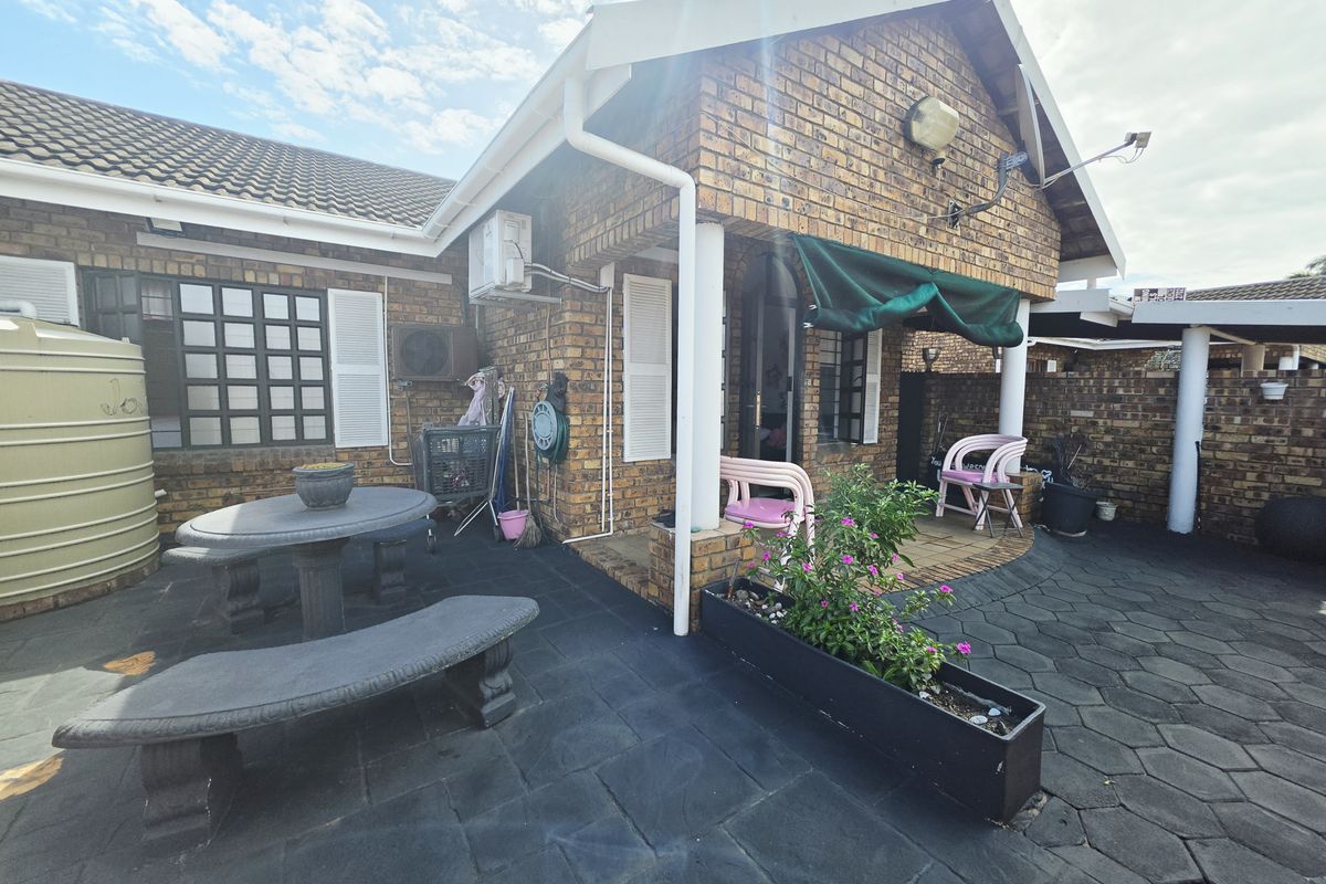 Rear exterior view of the townhouse featuring a paved patio area, face brick facade, water storage tank, and installed air conditioning unit.