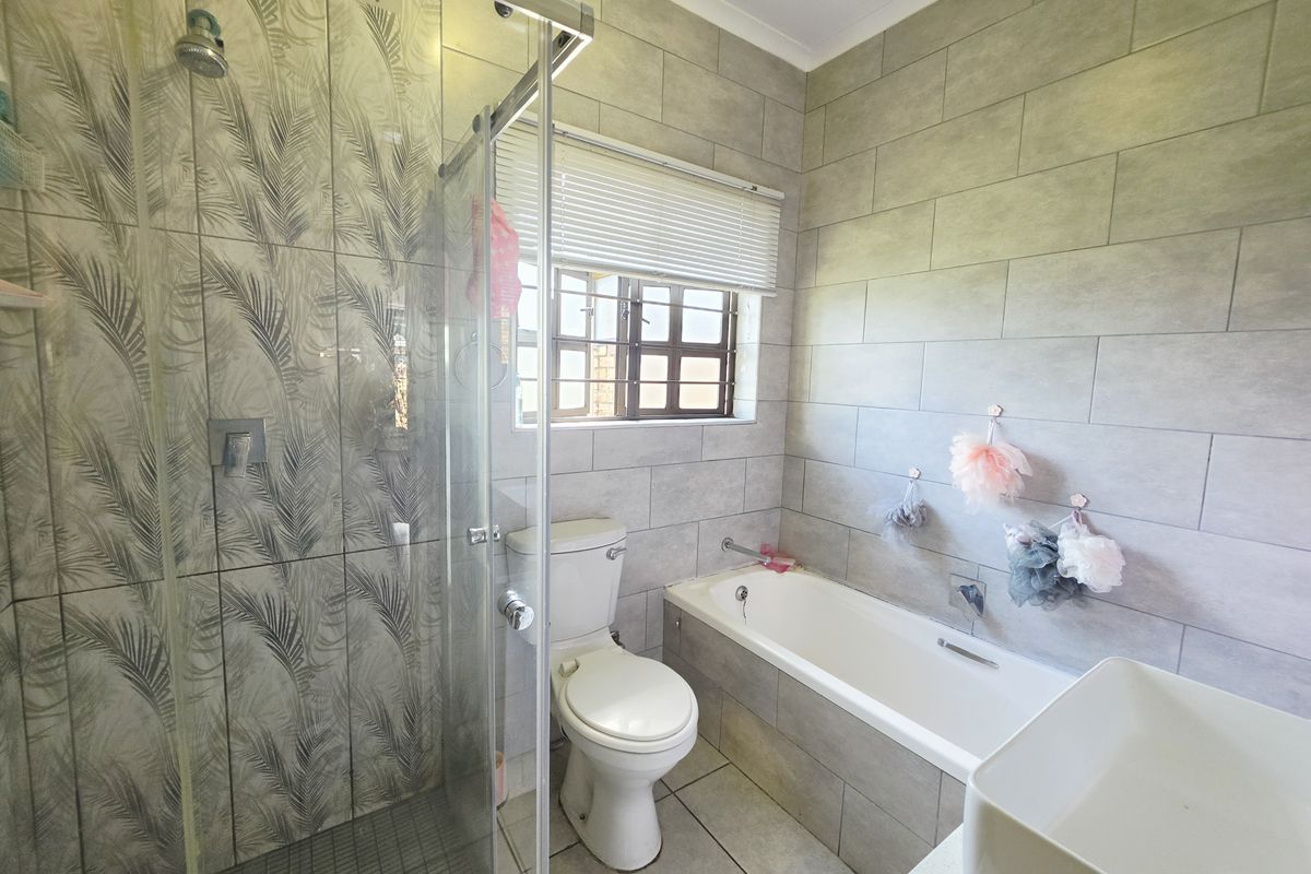 A modern bathroom featuring a glass-enclosed shower, a built-in bathtub, and neutral grey wall tiling with a decorative feature wall in the shower area.