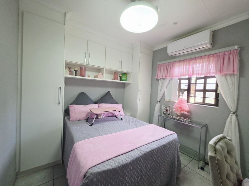 A well-maintained bedroom featuring built-in cupboards, overhead storage cabinetry, tiled flooring, and a split-system air conditioner for climate control.