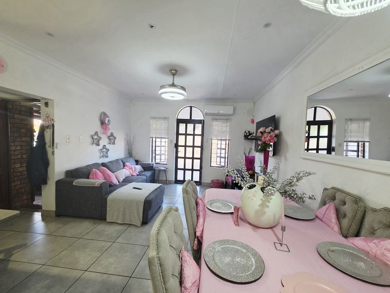 Open-plan living and dining area featuring tiled flooring, a ceiling fan, and a split-system air conditioner with access to an arched exterior door.