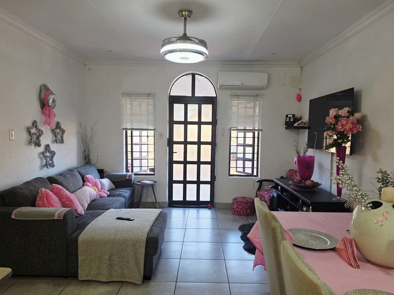Open-plan living and dining area featuring ceramic tiled flooring, a ceiling fan, split system air conditioning, and an arched glass panel entrance door.