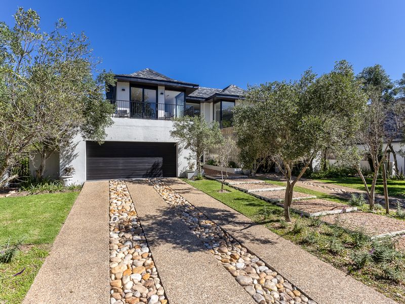 A modern double-story residence featuring a well-maintained pebble driveway, integrated double garage, and an upper-level balcony set within a landscaped garden.