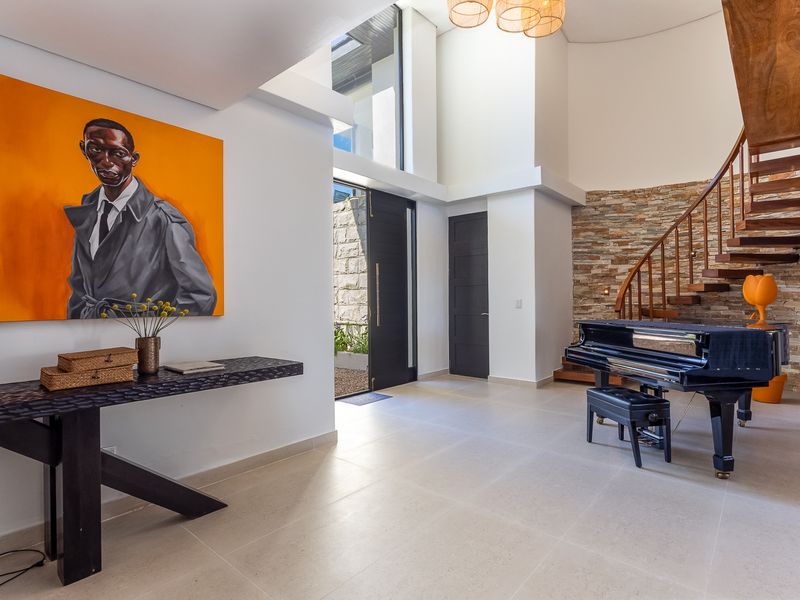 Spacious double-volume entrance hall featuring a striking stone feature wall, elegant wooden staircase, and modern tiled flooring with a grand pivot front door.