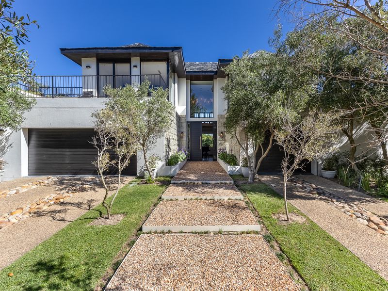 A modern double-story residence featuring stone cladding, a double garage, a balcony with metal railings, and a well-maintained landscaped front garden.