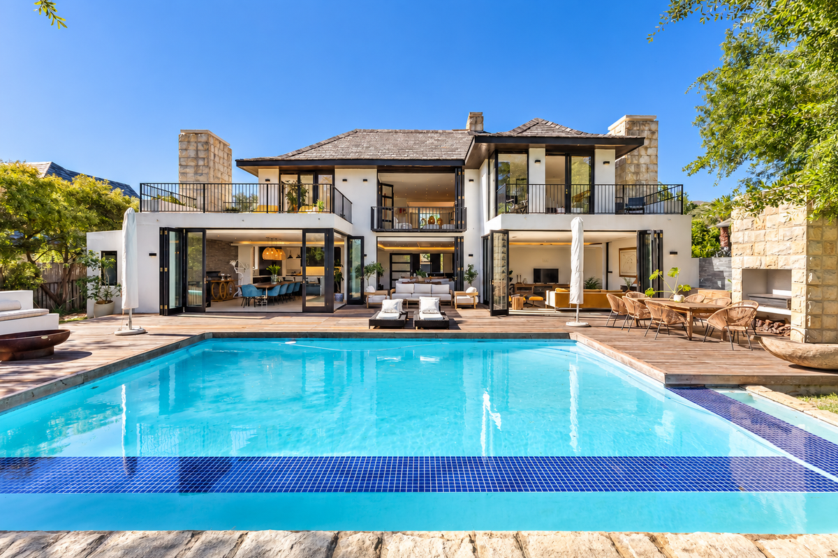 A stunning rear exterior view featuring a large swimming pool, expansive timber decking, and a modern home with bi-fold doors and stone-clad architectural details.
