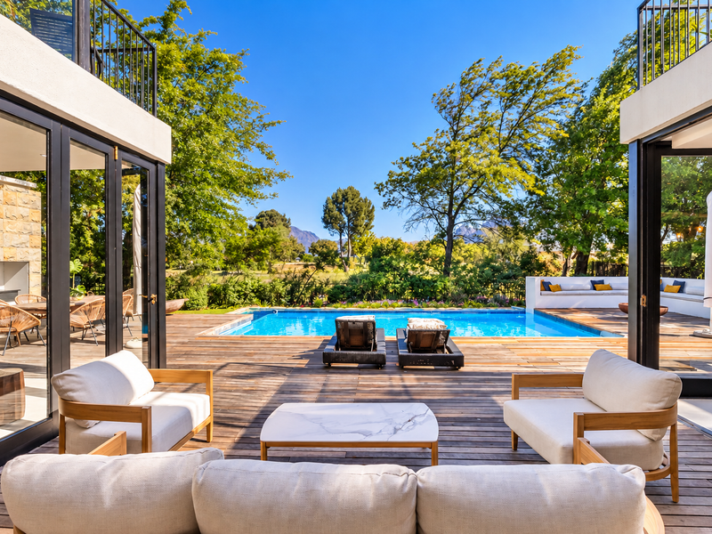 A luxurious outdoor pool area featuring extensive timber decking, built-in seating, and seamless indoor-outdoor flow through large bi-fold doors overlooking the garden.