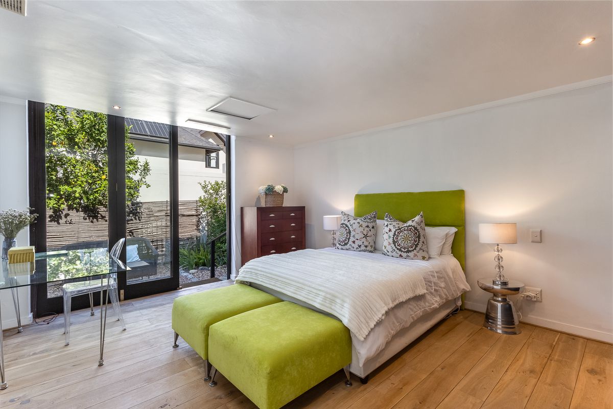 A bright and modern bedroom featuring hardwood flooring, recessed lighting, and large sliding glass doors that provide direct access to the outdoor area.