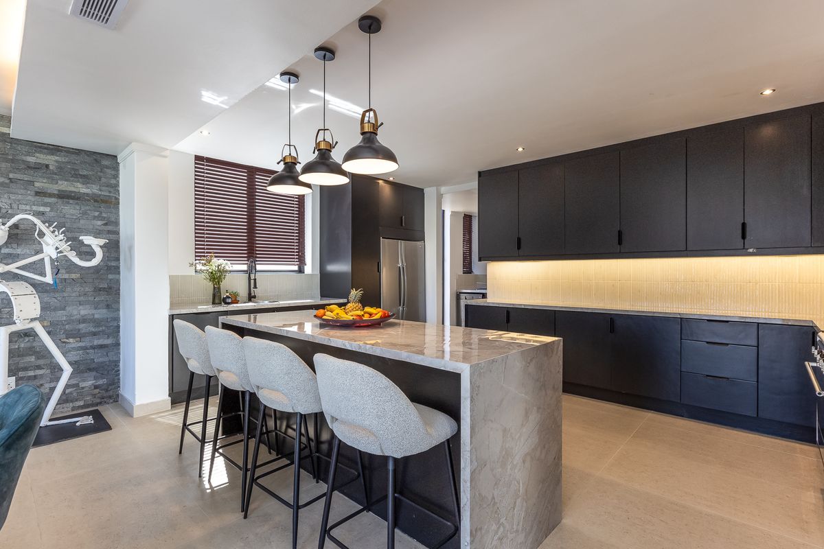 Modern kitchen featuring a large stone island, matte black cabinetry, under-cabinet lighting, and a striking stacked stone feature wall.