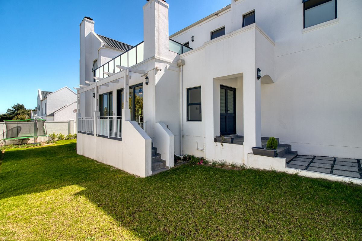 Rear view of the property featuring a raised patio with a pergola, glass balustrade, and direct access to the landscaped garden.