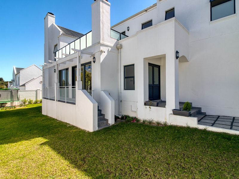 Rear view of the property featuring a raised patio with a pergola, glass balustrade, and direct access to the landscaped garden.