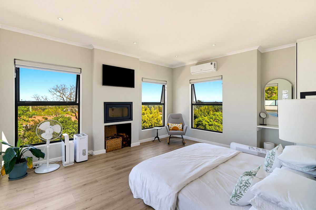 Spacious bedroom featuring modern laminate flooring, a built-in fireplace, split-system air conditioning, and large windows offering scenic views.