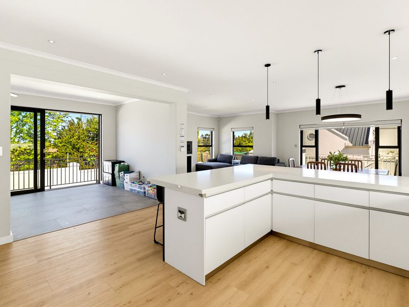 Spacious open-plan living area featuring a modern kitchen island, sleek cabinetry, and seamless flow to an outdoor balcony through large sliding glass doors.