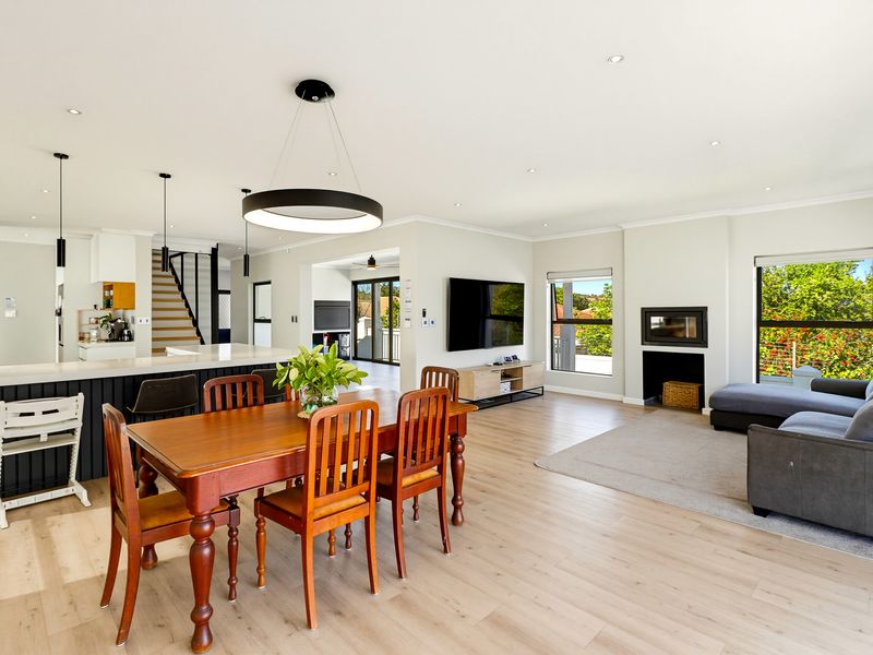 Spacious open-plan living and dining area featuring modern laminate flooring, a built-in fireplace, and a sleek kitchen island with pendant lighting.